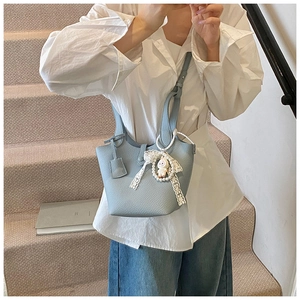 Close-up of light blue lychee pattern leather bucket bag with doll and lace charm details