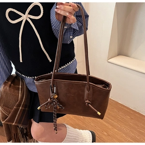 Dettaglio di una borsa tote marrone vintage con trama in pelle e ciondolo intrecciato