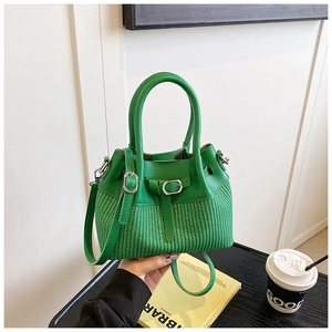 Detail view of bright green bucket bag with woven texture and premium metal buckle accents