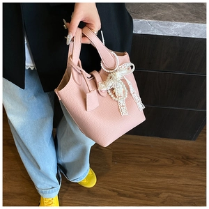 Detailed shot of pink pebble leather bucket bag featuring lace and pearl bow accent