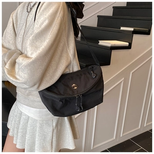 Detail of black nylon crossbody bag featuring double zippers and round metal logo accent