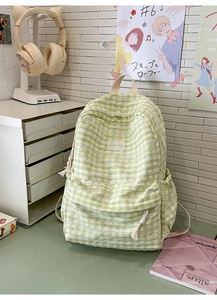 Detail of light green plaid backpack with zippered pocket and logo tag on a desk