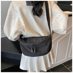 Detail of a black nylon crescent crossbody bag worn by a model in a minimalist room