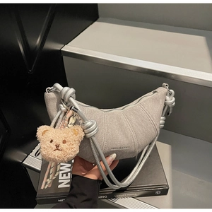 Detail der grauen Croissant-Tasche mit dickem Seilriemen und süßem Teddybär-Anhänger