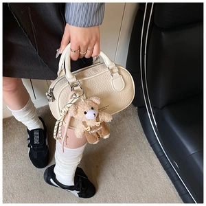 Detail of off-white lychee texture leather bowling bag with cute plush bear charm accessory