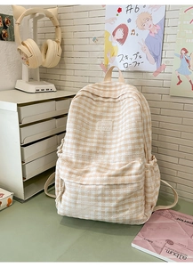 Detail of light orange plaid backpack with lace trim and brand logo on a desk