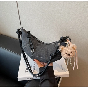 Detail der dunkelgrauen Denim-Croissant-Tasche mit vertikalen Nähten und Bären-Anhänger