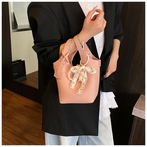 Detail of pink lychee leather bucket bag with lace bow, pearl charm, and bear pendant