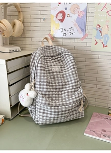 Detail of plaid backpack featuring delicate white lace trim and a cute plush bunny charm