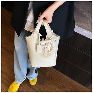 Detail of beige bucket bag featuring lacy bow and cute bunny charm on textured leather