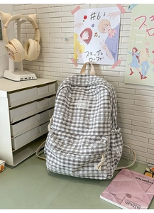 Detail of grey plaid backpack featuring a front zipper pocket and woven rope puller