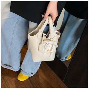 Detail of cream white pebbled leather bucket bag with lace bow and cute charm