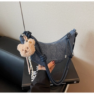 Detail der dunkelblauen Denim-Croissant-Tasche mit Reißverschluss und Plüschbär-Anhänger