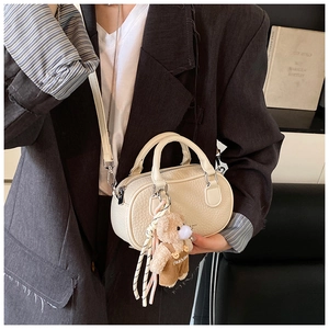 Detail of cream bowling bag with lychee texture and brown plush bear charm