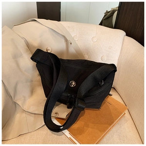 Detail of black canvas crossbody bag with silver logo on a modern lounge chair