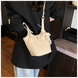Detail of beige bucket bag featuring litchi texture and elegant pearl bow charm