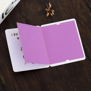 Detail of purple folded greeting card with white laser-cut hollow sleeve on wood surface