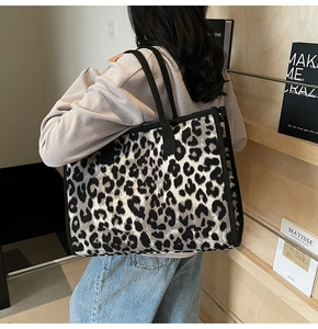 Close-up of a large leopard print tote bag with black trim worn on a model's shoulder