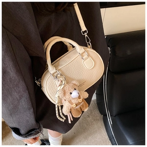 Close-up of off-white lychee leather bowling bag with cute plush bear charm detail