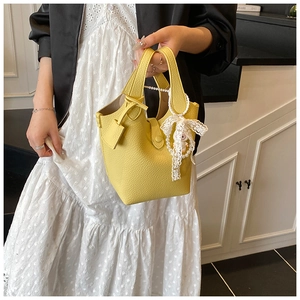 Close-up of yellow leather bucket bag with white lace bow and pearl pendant detail