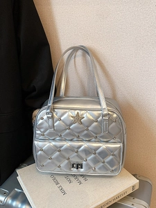 Silver quilted tote bag with star logo and rivets placed on a metallic suitcase
