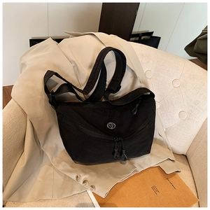 Close-up of black canvas hobo bag with dual zippers and round metal logo on beige blazer