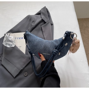 Detail der blauen Denim-Hörnchentasche mit Steppung und braunem Plüschbären-Anhänger