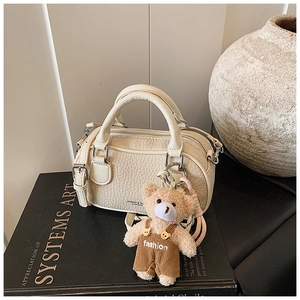 Close-up of beige leather bowling bag with teddy bear charm on black books
