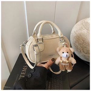 Close-up of cream textured leather Boston bag with a cute plush bear charm accessory