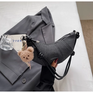Detail der dunkelgrauen Denim-Halbmondtasche mit Nähten und braunem Teddybär-Anhänger