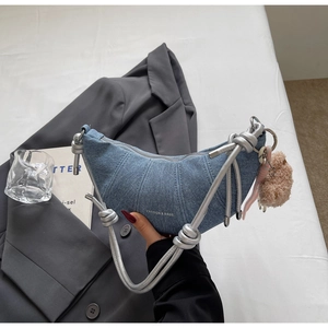 Detail der blauen Jeans-Halbmondtasche mit silbernem Gurt und Plüschbär-Anhänger
