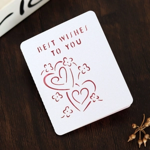Detail view of laser-cut white card with Best Wishes text and heart motifs on wood
