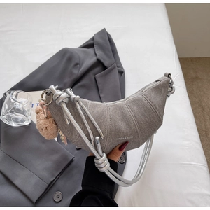 Detail der grauen sichelförmigen Schultertasche mit Metallseil und Bärenanhänger