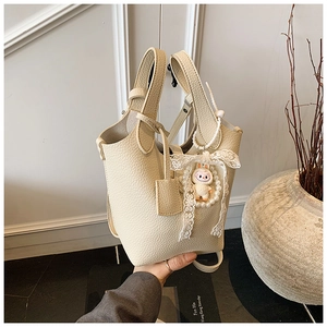 Detail of off-white lychee pattern leather bucket bag with pearl and lace bow charm