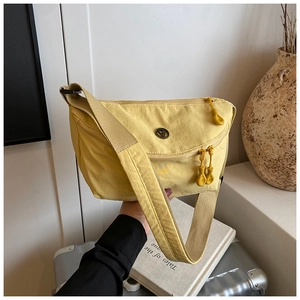 Detail of a bright yellow nylon crossbody bag with metal logo and teardrop zippers