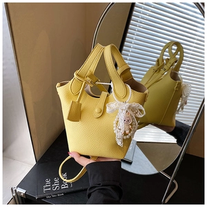 Detailed close-up of a yellow bucket bag with lychee texture and pearl bow charm