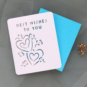 Detail showing laser-cut Best Wishes text and heart patterns on card with blue envelope