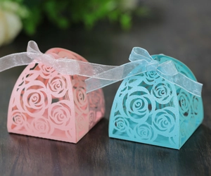 Close-up of laser-cut rose hollow favor boxes with silk ribbons on a wooden surface
