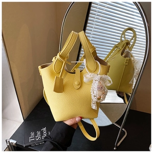 Detail of yellow lychee leather bucket bag with lace bow and cute doll pendant