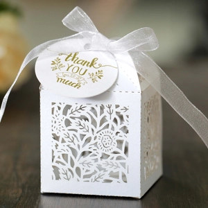 White laser cut floral wedding favor box with a gold thank you tag and white organza ribbon