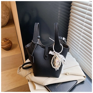 Detail of black lychee grain leather bucket bag with elegant pearl and lace charms