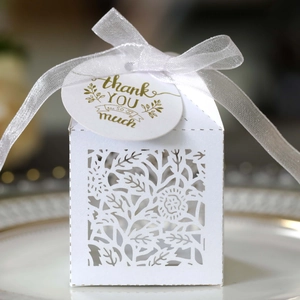 Close-up of laser-cut white favor box with white ribbon and gold thank you tag