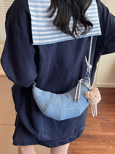 Croissant-Tasche aus Denim mit weißem Text und rosa Bärenanhänger an einem Model