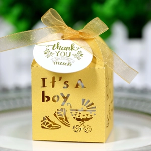 Macro detail of yellow 'It's A Boy' favor box with laser-cut design and gold ribbon bow