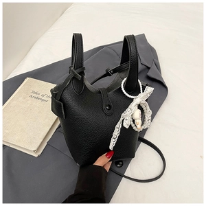 Detail of black lychee texture bucket bag with lace pearl bow charm and shoulder strap