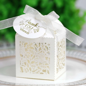 Detail of white laser-cut candy box with floral patterns, white ribbon and thank you tag