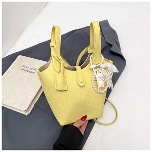 Close-up of bright yellow litchi grain bucket bag with a pearl rabbit charm accessory