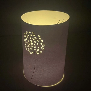 Detail of white paper lamp shade with laser-cut dandelion patterns and warm LED glow