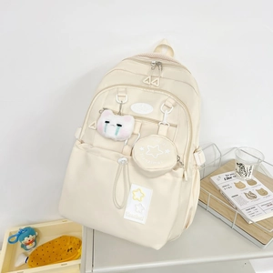 Détail du sac à dos scolaire crème avec patchs étoiles et porte-clé chat en peluche