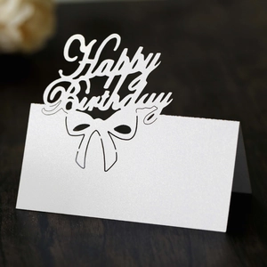 Laser-cut white Happy Birthday place card with a bow design on a dark wood background